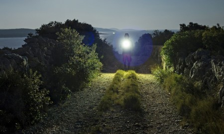 Man walking on road with flash light at night under the moon close the Adriatic Sea in Croatia. Calm, peaceful and mystical image.