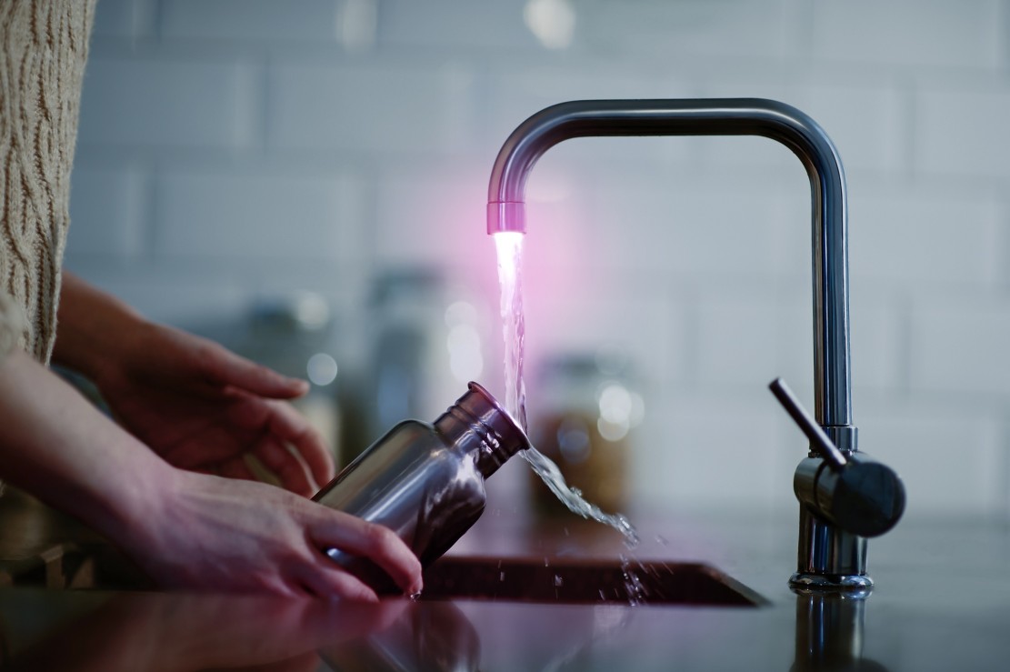 A woman cleans a plastic free and reusable water bottle in a kitchen sink, close up.