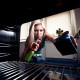 young blond holding a sponge & cleaner and looking into the oven